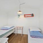 Two single beds, nightstand, and wall shelf with books.