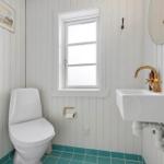 Bathroom with toilet, sink, and window. Panelled walls and turquoise floor.