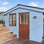 A small blue wooden house with brown door and windows. Wooden terrace with steps.