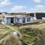 Blue house with red text on the facade, surrounded by dunes and other houses.