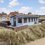 A light blue beach house with terrace and seating area between dunes.