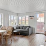 Living and dining area with sofa, table, chairs, and wood stove. Windows and door show outdoor area.