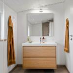 Badezimmer mit Waschbecken, Spiegel und Dusche. Holzschrank, Fenster und Handtücher.
