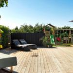 Holzterrasse mit Liegestühlen, Spielplatz und Grillbereich im Garten.