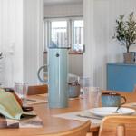 Esstisch mit Tassen, Gläsern und Kaffeekanne. Hintergrund: blaue Kommode und Pflanzen.