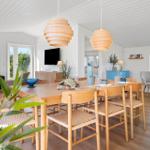 Esszimmer mit Holztisch, Stühlen und hängenden Lampen. Wohnbereich mit Sofa und TV.