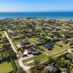 Aerial view of coastal village with houses, green lawns, and ocean in background.