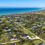 Aerial view of coastal village with houses, greenery, and ocean shoreline.
