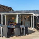 Terrasse mit Tisch, Stühlen und Sonnenschirm. Hintergrund: offene Haustür und Küche.