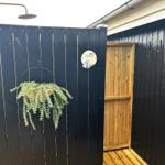 Außenbad mit Dusche, Pflanze und Holztür.