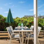 Terrasse mit Tisch, Stühlen und grünem Sonnenschirm. Hintergrund: grüne Hecke mit rosa Blüten.