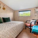 Schlafzimmer mit Bett, Stuhl und Fenster mit Blick auf Grün.