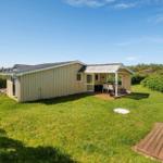 Ein Haus mit Terrasse, Garten und blauem Himmel. Blumen und Gras sind sichtbar.