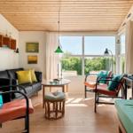 Wohnzimmer mit Holzdecke, Sofa, Sesseln und großem Fenster mit Blick auf Grün.