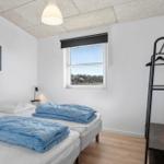 Two beds with blue blankets, window with view of landscape, black coat rack and wall picture.