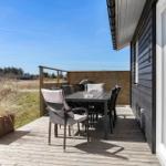 Deck with table, chairs, and grill. Wooden railing and plant. View of field and forest.
