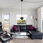 Living room with black leather sofa, glass table, and seating. Large windows and door with view of outdoor area.