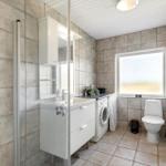 Bathroom with shower, washing machine, and toilet. Tiled walls and window.
