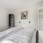 Bedroom with bed, white shelves, and wall art. Ceiling with wooden planks.