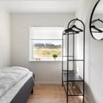 Bedroom with bed, clothing rack, and window overlooking green area.