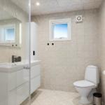 Badezimmer mit Toilette, Waschbecken und Dusche. Fenster und Spiegel sichtbar.