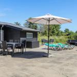 Terrasse mit Tisch, Stühlen, Sonnenschirm und Liegestühlen neben einem Haus.
