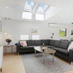 Wohnbereich mit grauem Sofa, ovalen Tisch und Dachfenstern. Küche im Hintergrund.