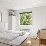 Schlafzimmer mit Bett, Schreibtisch und Fenster mit Blick auf Bäume.