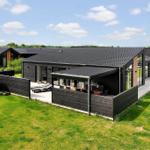 Moderne Villa mit Terrasse, Liegen und Holzsauna auf grünem Grund.