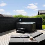 Terrasse mit Whirlpool und Liegen. Schwarze Holzwand und grüner Garten im Hintergrund.