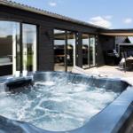 Außenbereich mit Whirlpool, Terrasse und Sitzgruppe. Schwarze Holzfassade und Glastüren.