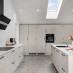 Moderne Küche mit hellen Schränken, Arbeitsplatten und Dachfenster. Einbauküche mit Spüle und Backofen.