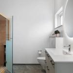 Badezimmer mit Sauna, Waschbecken und Toilette. Rundes Spiegel mit Beleuchtung.