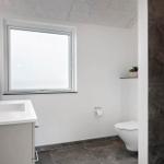 Badezimmer mit Waschbecken, Toilette und Fenster. Duschbereich mit dunkler Wandverkleidung.