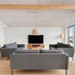Wohnzimmer mit grauen Sofas, Holzboden und Backsteinwand. Fernseher und Beleuchtung sichtbar.