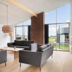 Wohnzimmer mit grauen Sofas, Holzboden und großen Fenstern zur Außensicht.