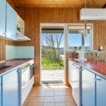 Kitchen with blue cabinets, red countertop, and wooden walls. Passage to terrace with view of greenery.