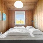 Bedroom with wooden walls, bed, and window. Ceiling light and wall art.
