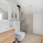 Badezimmer mit Dusche, Waschbecken und Toilette. Weiße Wände und Holzelemente.