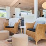Zwei geflochtene Sessel mit Felldecken und Kissen stehen vor Fenstern mit Holzwand.