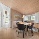 Essbereich mit runden Tisch und vier Stühlen. Holzwände und -decke. Fenster mit weißen Vorhängen.
