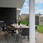 Patio with table, chairs, and grill under cover. Lawn and wooden fence in background.