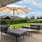 Terrace with umbrella and two loungers on paved ground. Green lawn and hedge in the background.