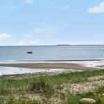 A small boat is on the water. Grass and sand are visible in the foreground.