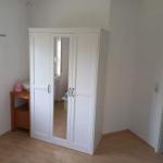Schlafzimmer mit weißem Kleiderschrank und Holzboden. Neben dem Schrank steht ein kleiner Holztisch.