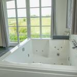 Whirlpool-Bad mit Blick auf grünes Feld durch große Fenster.