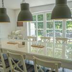 Esszimmer mit langem Tisch, weißen Stühlen und großen Fenstern zur Terrasse.