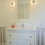 Bad mit Waschbecken, Spiegel und Dusche. Wandverkleidung mit Streifenmuster.