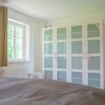 Schlafzimmer mit Bett, Kleiderschrank und Fenster mit Blick auf Grün.