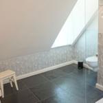 Badezimmer mit Dusche, Toilette und Waschbecken unter Dachschrägen.